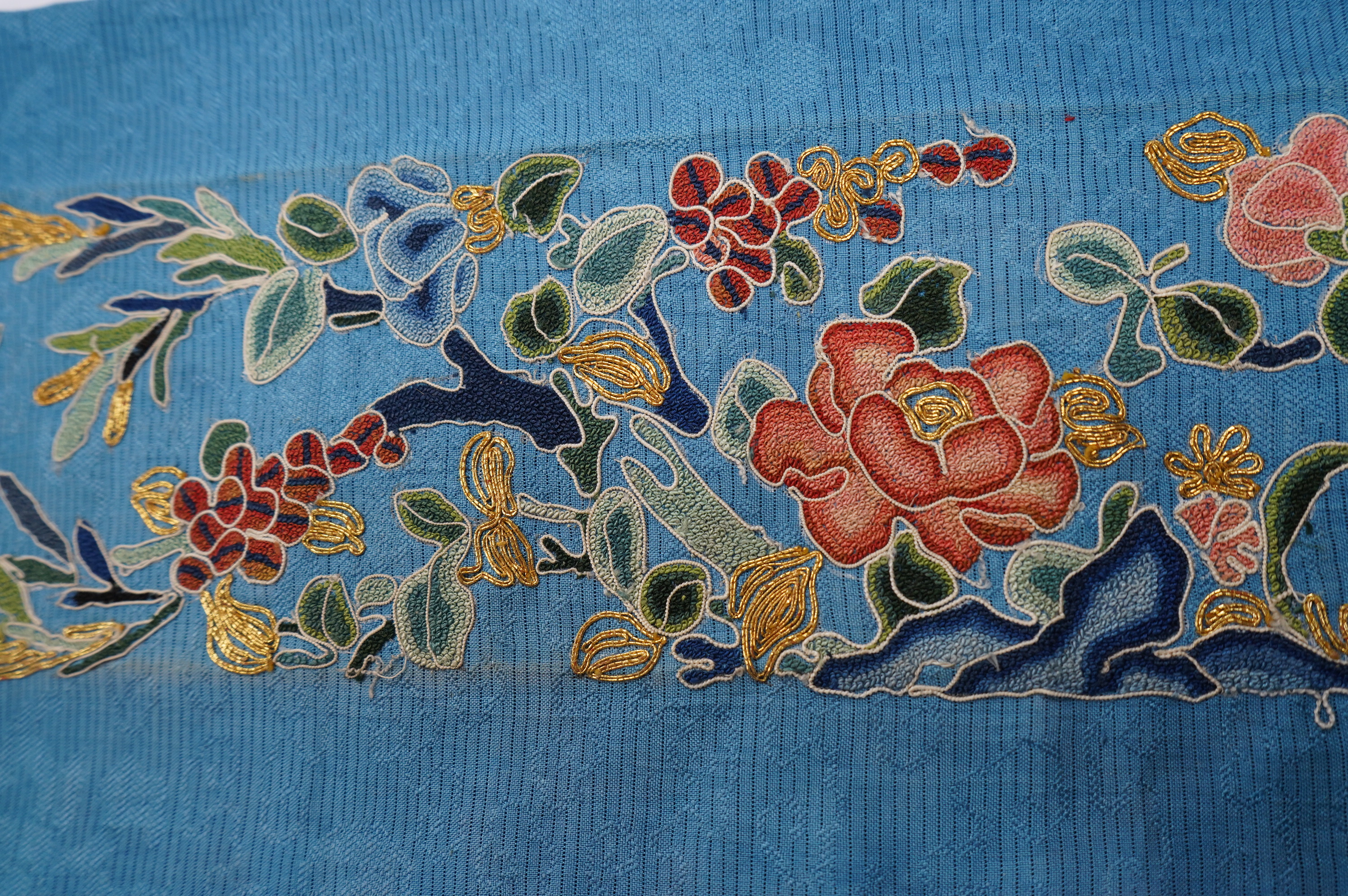 A 19th century Chinese blue silk embroidered sleeve band, embroidered in multi-coloured silk and gold thread, mostly worked in Chinese knot, in a floral and bat design, 48cm long, unframed., Condition - good